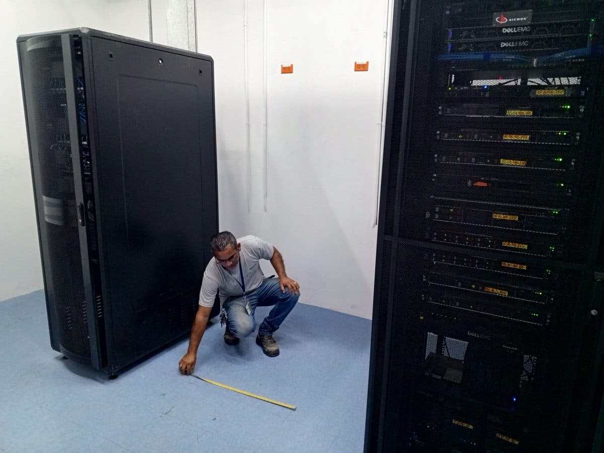 Técnico midiendo frente a racks de comunicaciones en una sala técnica.
